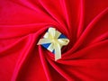 Blue Gift box with yellow ribbon on center of spiral red silk background. Royalty Free Stock Photo