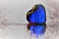 Blue glass heart on shiny silver table Royalty Free Stock Photo