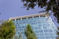 Close up view of a blue glass window skyscraper from a street view wit trees int eh foreground