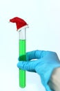 A blue-gloved hand holds a test tube with a green solution with a decorative red cap in the chemical laboratory