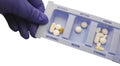 Blue gloved hand showing tablets in daily pill box isolated