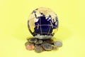 Blue and gold globe sitting on top of a pile of a mixture of coins from the US Europe and Britain