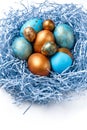 Blue and golden modern easter eggs in a nest on a white background.