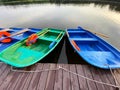 Blue and green boats with oars and orange lifebuoys are moored to a wooden pier