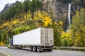 Blue and green classic big rig semi truck transporting cargo in reefer semi trailer moving on the highway road driving past a Royalty Free Stock Photo