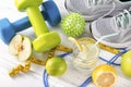 Blue and green dumbbells, a glass of water with lemon, gray sneakers, ball, Apple, skipping rope, measuring tape on a white