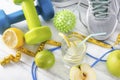 Blue and green dumbbells, glass of water with lemon, gray sneakers, ball, measuring tape on a white background