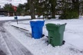 A blue and a green trash can covered with snow by the side of a snow covered, freshly plowed street waiting for garbage pickup Royalty Free Stock Photo