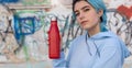 Blue haired Teenage girl in blue hoodie staying near graffiti wall with red water bottle Royalty Free Stock Photo