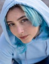 Blue haired Teenage girl in light blue oversize hoodie lookinginto a camera from down