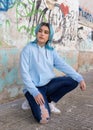 Blue haired Teenage girl in light blue oversize hoodie sitting on her haunches near graffiti wall Royalty Free Stock Photo