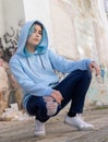 Blue haired Teenage girl in light blue oversize hoodie sitting on her haunches near graffiti wall Royalty Free Stock Photo