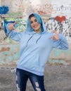 Blue haired Teenage girl staying against graffiti wall and pointing in center of blue hoodie