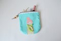 Blue handmade zipper pouch with cute doll, hair pins, mascara and hair tweezers over white