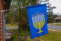 Blue hanukkah flag with a picture of a menorah on it hanging from a flagpole attached to the front of a house