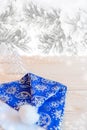 Blue hat Santa Claus on wooden table on background of snow-covered pine branches. Royalty Free Stock Photo