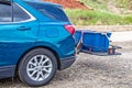 Blue hatchback car parked on gravel with hitch cargo carrier holding tied down rubber storage box on back - Closeup and cropped