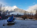 Blue helicopter parked in large meadow under the spectacular snowy mountains.