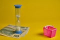 Blue hourglass and dollars with shopping basket at yellow background