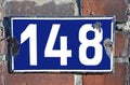 A blue house number plaque fixed on a brick wall, showing the number one hundred forty eight Royalty Free Stock Photo