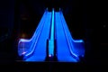 Blue illuminated escalator at night with intentional motion blur of the escalator steps