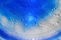Blue ink flows inside fizzy liquid with bubbles creating round layers macro bright wallpaper Royalty Free Stock Photo