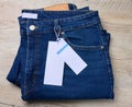 Blue jeans on a wooden surface. The pants are neatly folded, and there is a brown leather patch at the waist of the jeans