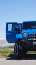 Blue Jeep Wrangler on a grassy hill with mountains in the background Royalty Free Stock Photo