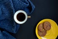 Blue knit sweater, gold cup with coffee and yellow plate with flavored cookies on dark black background Royalty Free Stock Photo