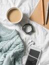 Blue knitted sweater, coffee with milk, notebook, headphones, smart phone on bed, top view. Women clothing