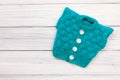 Blue knitted vest for baby on white wooden background