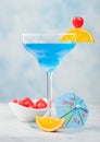 Blue lagoon summer cocktail in margarita glass with sweet cocktail cherries and orange slice with umbrella on blue background Royalty Free Stock Photo