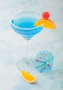 Blue lagoon summer cocktail in margarita glass with sweet cocktail cherries and orange slice with umbrella on blue background Royalty Free Stock Photo