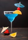 Blue lagoon summer cocktail in margarita glass with sweet cocktail cherries and orange slice with umbrella on dark background Royalty Free Stock Photo