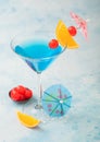 Blue lagoon summer cocktail in martini glass with sweet cocktail cherries and orange slice with umbrella on blue background Royalty Free Stock Photo