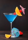 Blue lagoon summer cocktail in martini glass with sweet cocktail cherries and orange slice with umbrella on dark background Royalty Free Stock Photo