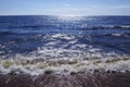 Blue lake, glare on the water, foaming wave comes ashore.