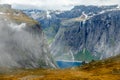 Blue lake surrounded by steep cliffs hiding in clouds, Trolltunga trail, Odda, Hordaland county, Norway Royalty Free Stock Photo