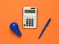 A blue light bulb, a blue pen and a calculator on an orange background Royalty Free Stock Photo