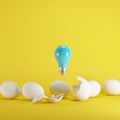 Blue light bulb floating from white eggshell and white eggs on yellow background. Royalty Free Stock Photo