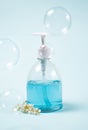 Blue liquid soap in dispenser with blooming twig and soap bubbles on light background