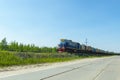 A blue locomotive tows a fuel tanks wagons against a blue sky.