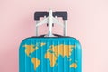 Blue luggage with world continents map and airplane toy on pastel rose background