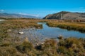 Blue marsh river flows among yellow grass with stone bank in Baikal mountains. Autumn landscape