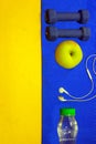 Blue mat, water, dumbbells, apple headphones, on a yellow background