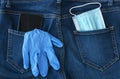 Blue medical mask, medical glove and black smartphone look out from back jeans pocket