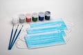 Blue medical masks lie on a white background together with paints for painting and brushes. Hobbies during self-isolation. Royalty Free Stock Photo