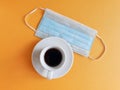 Blue medical protective mask and a cup of coffee on a yellow background. The concept of protecting your health.