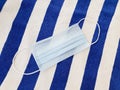 Blue medical protective mask on striped texture towel. Modern reality and relaxing on the beach during the coronavirus period