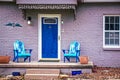 Blue mermaid adirondack chairs sit on porch of brick house painted purple with blue front door